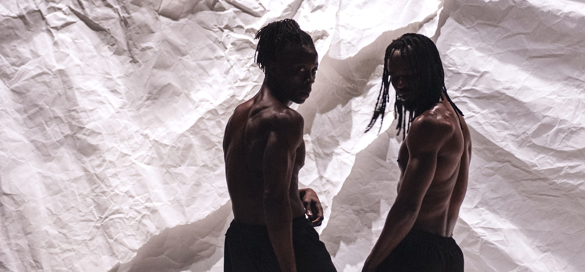 Two dancers pose in front a white fabric background