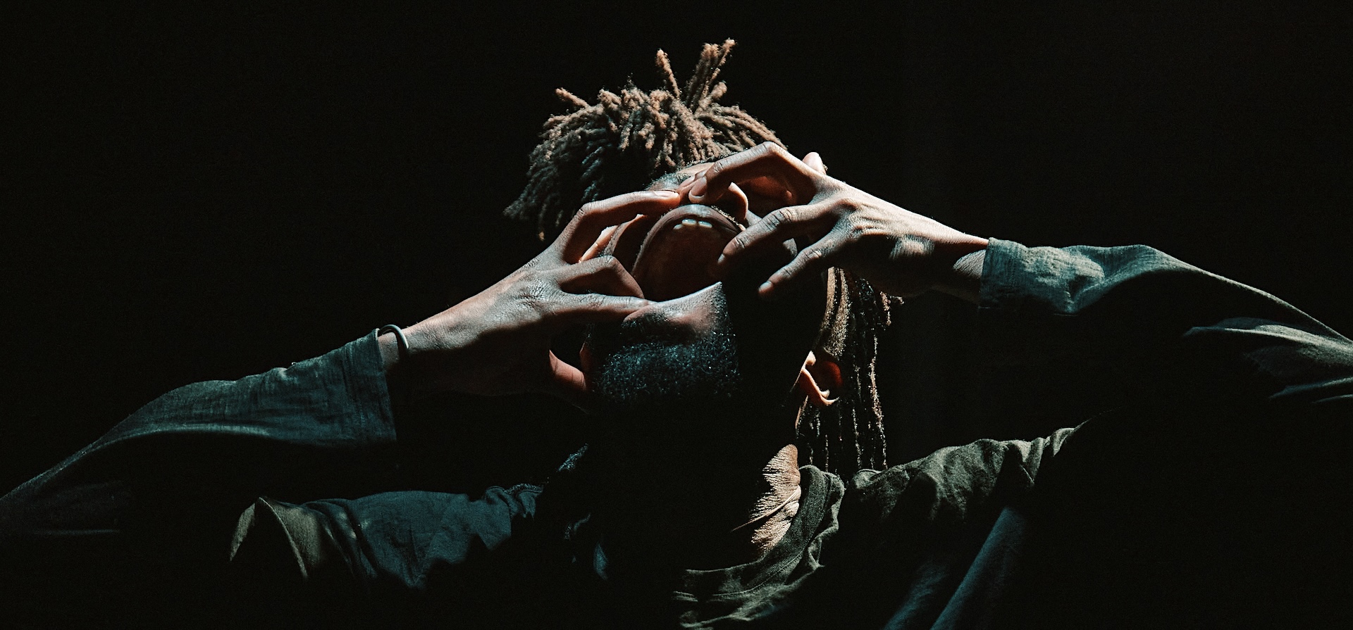A dancer with dreadlocks covers his face with his hands