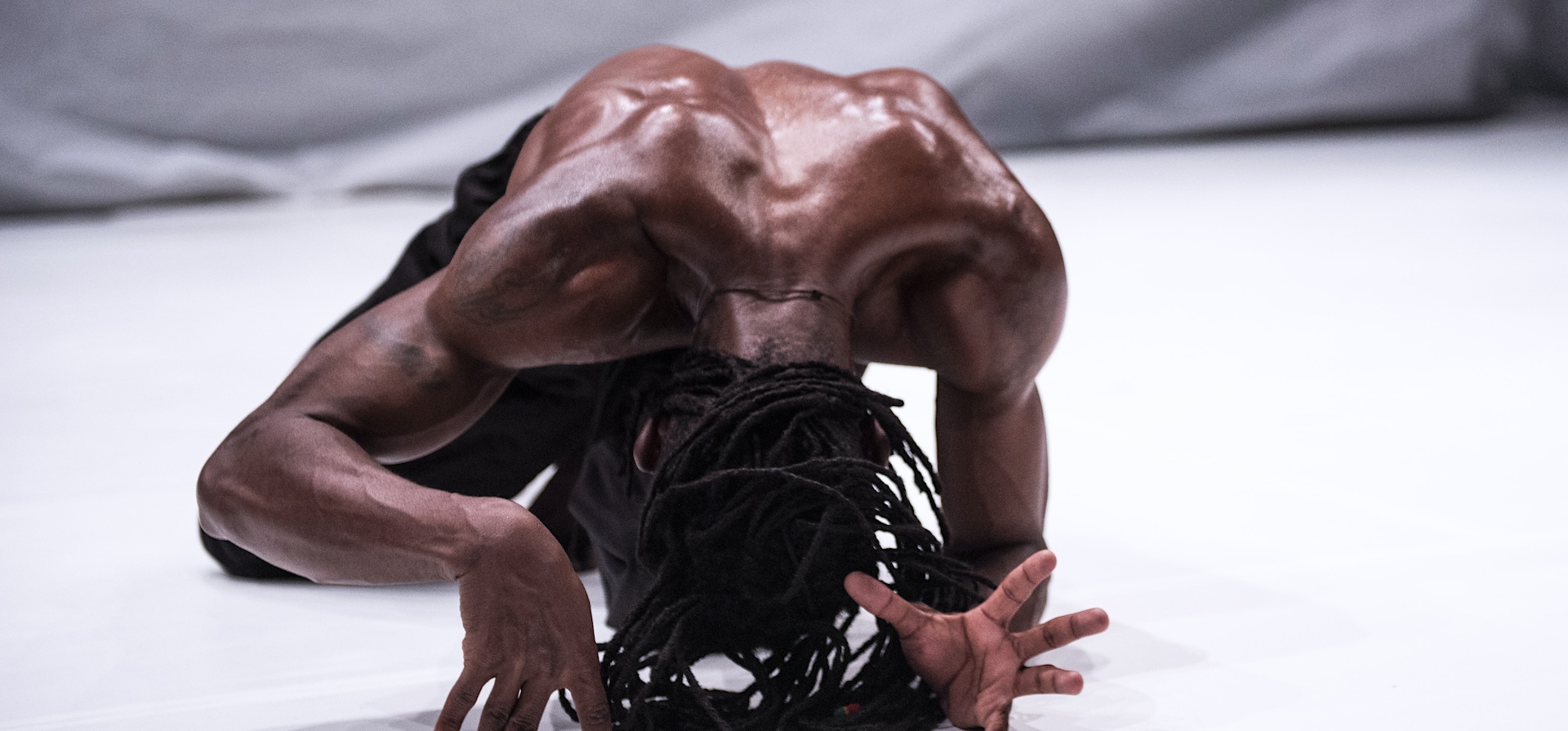 A black dancer with dreadlocks arches his back on the floor in the middle of dance routine