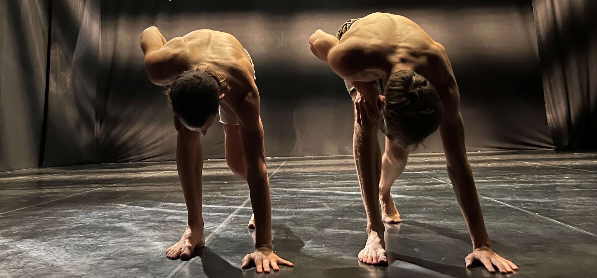 Two dancers each with one hand on the floor in a synchronised pose