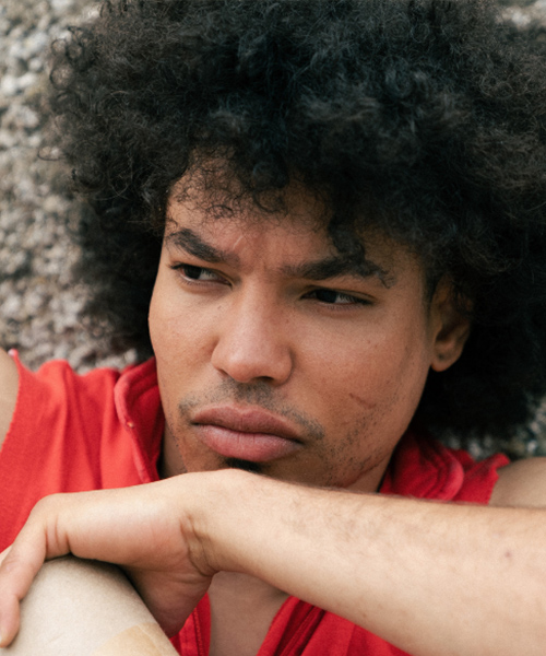 A profile picture of Cristian Enmanuel-Dirocie the dance artist. He is wearing a red t shirt and is looking off to the left of the camera