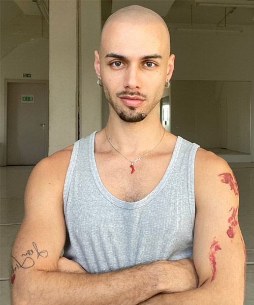 A headshot of Fabian Riess wearing a gray vest with his arms folded in front of him.