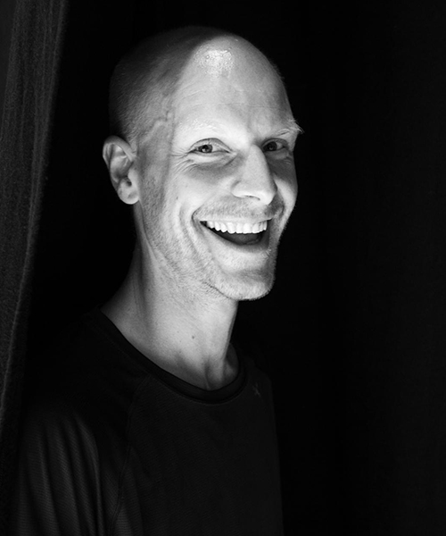 A picture of Ian Garside smiling at the camera in front of a dark background