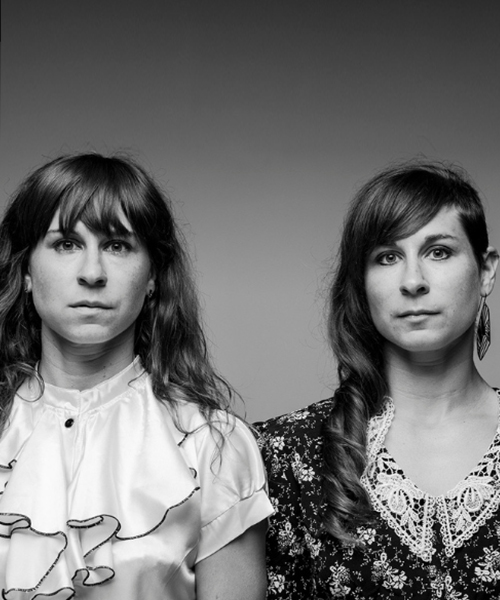 A picture of the two founding members of Junk Ensemble in black and white looking at the camera with neutral expressions