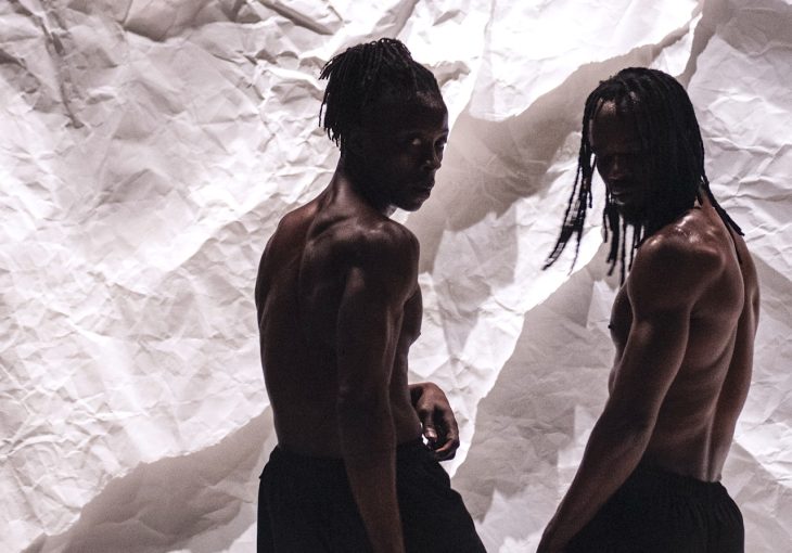 Two dancers pose in front a white fabric background