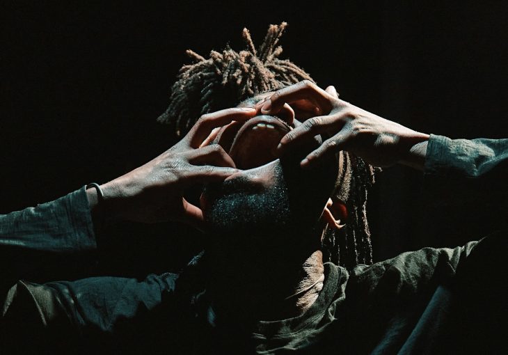 A dancer with dreadlocks covers his face with his hands