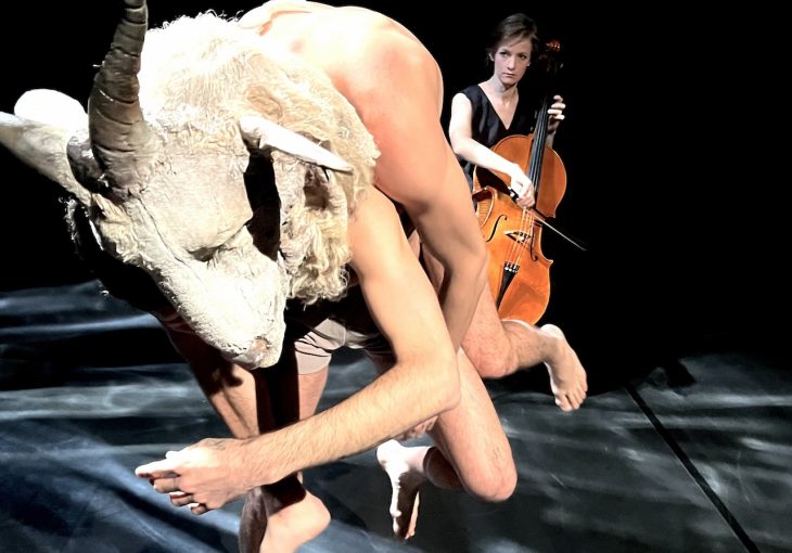 Up close of a dancer in an animal mask with a cello being played in the background