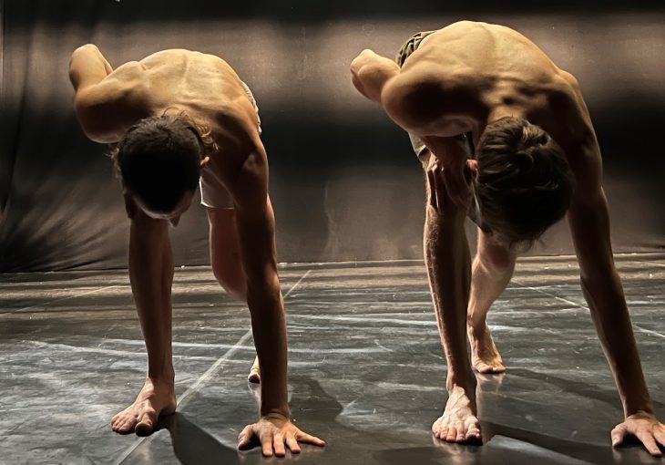Two dancers each with one hand on the floor in a synchronised pose
