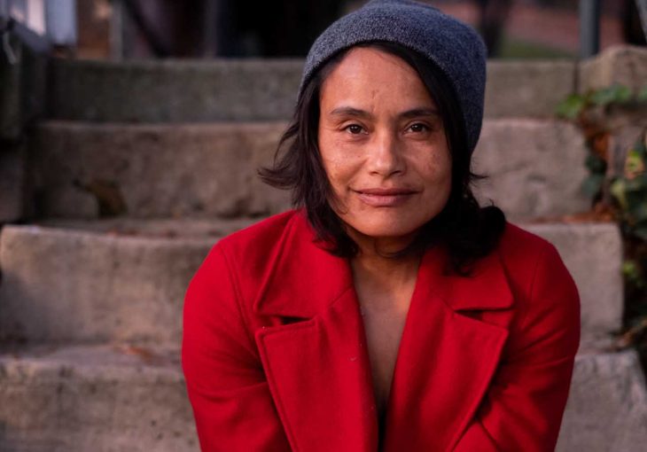 A headshot of Murielle Elizéon in a red coat sitting on concrete steps